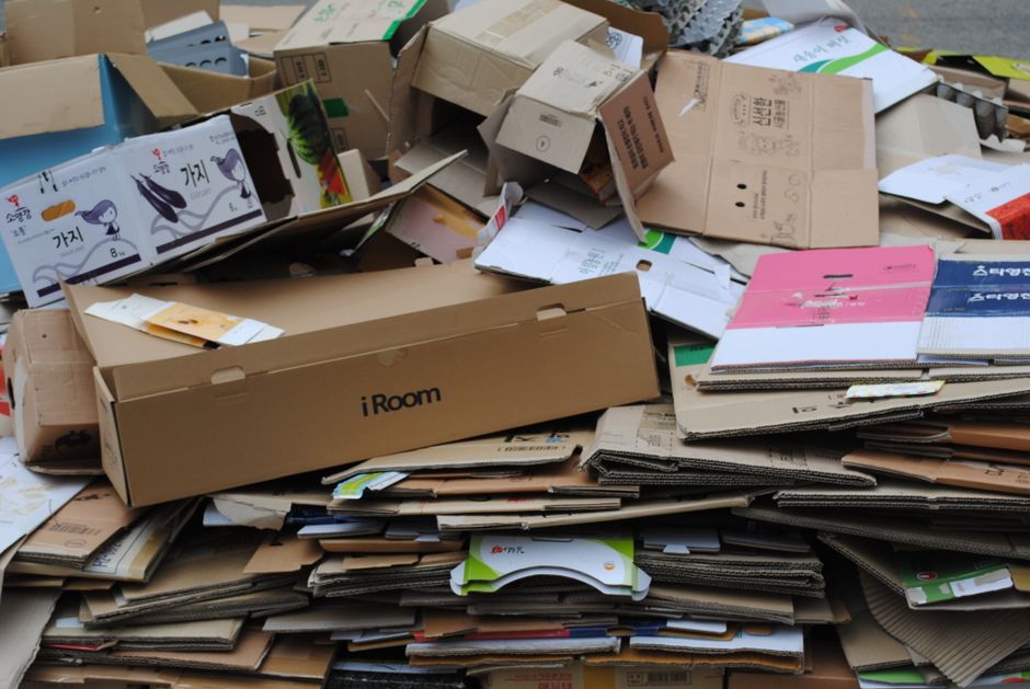 Two individuals are engaged in what appears to be a cleanup or disposal activity outside a fruit shop. The woman on the left, dressed in a patterned dress, is inspecting or handling items from an open
